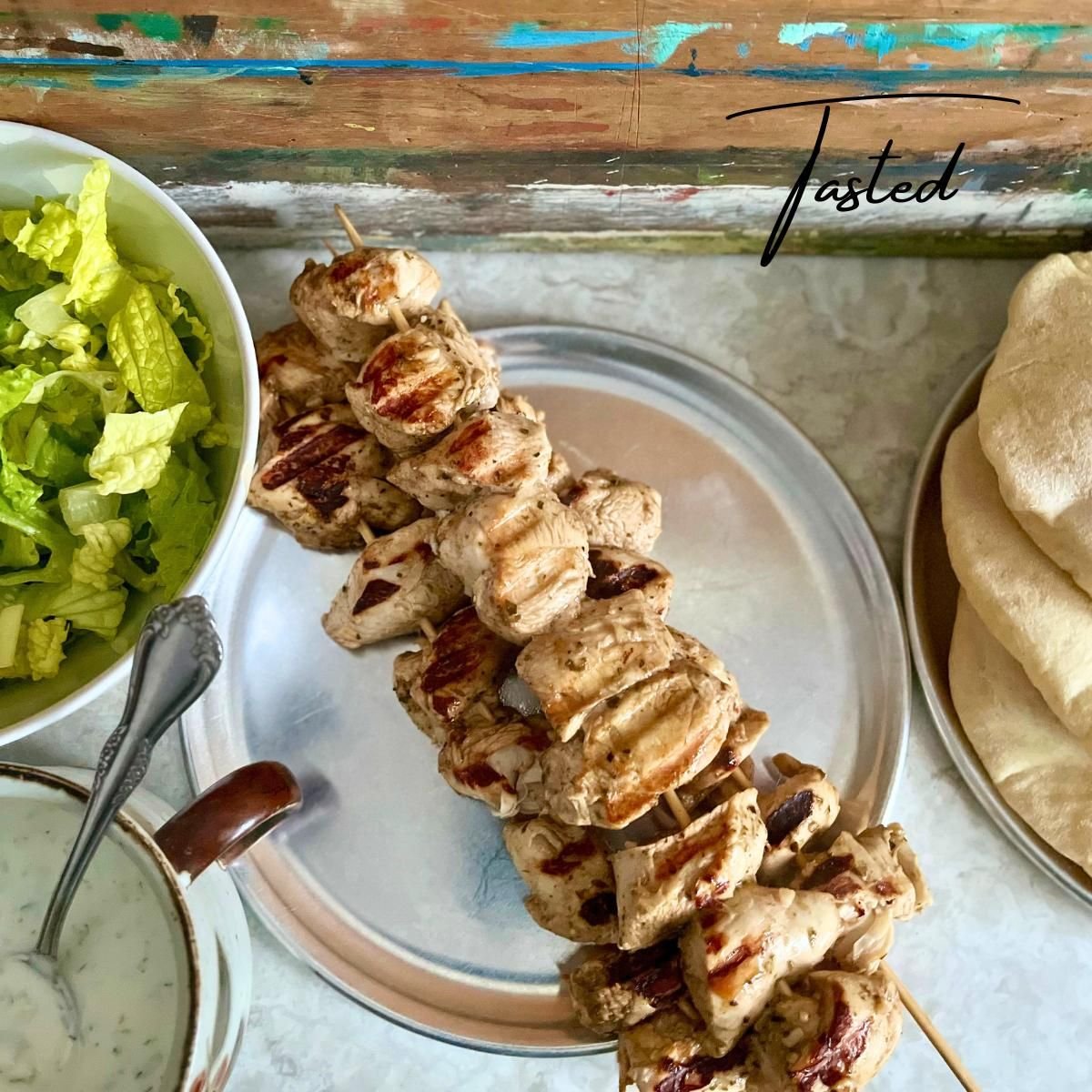 Grilled chicken souvlaki skewers on a metal platter with pita bread, salad and tzatziki