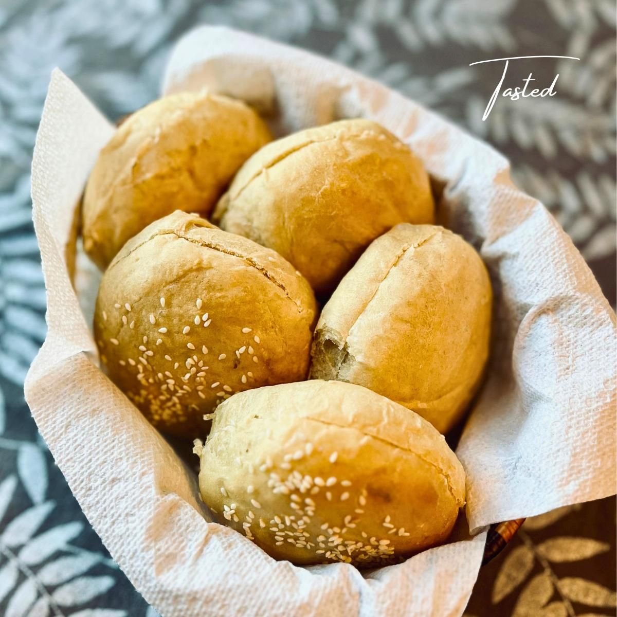 Basket of golden homemade hamburger buns topped with sesame seeds