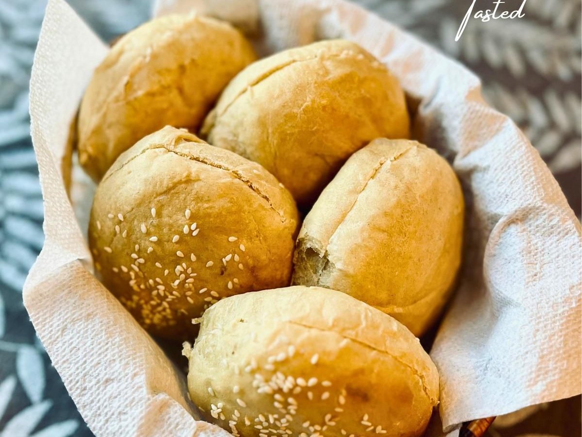 Basket of golden homemade hamburger buns topped with sesame seeds