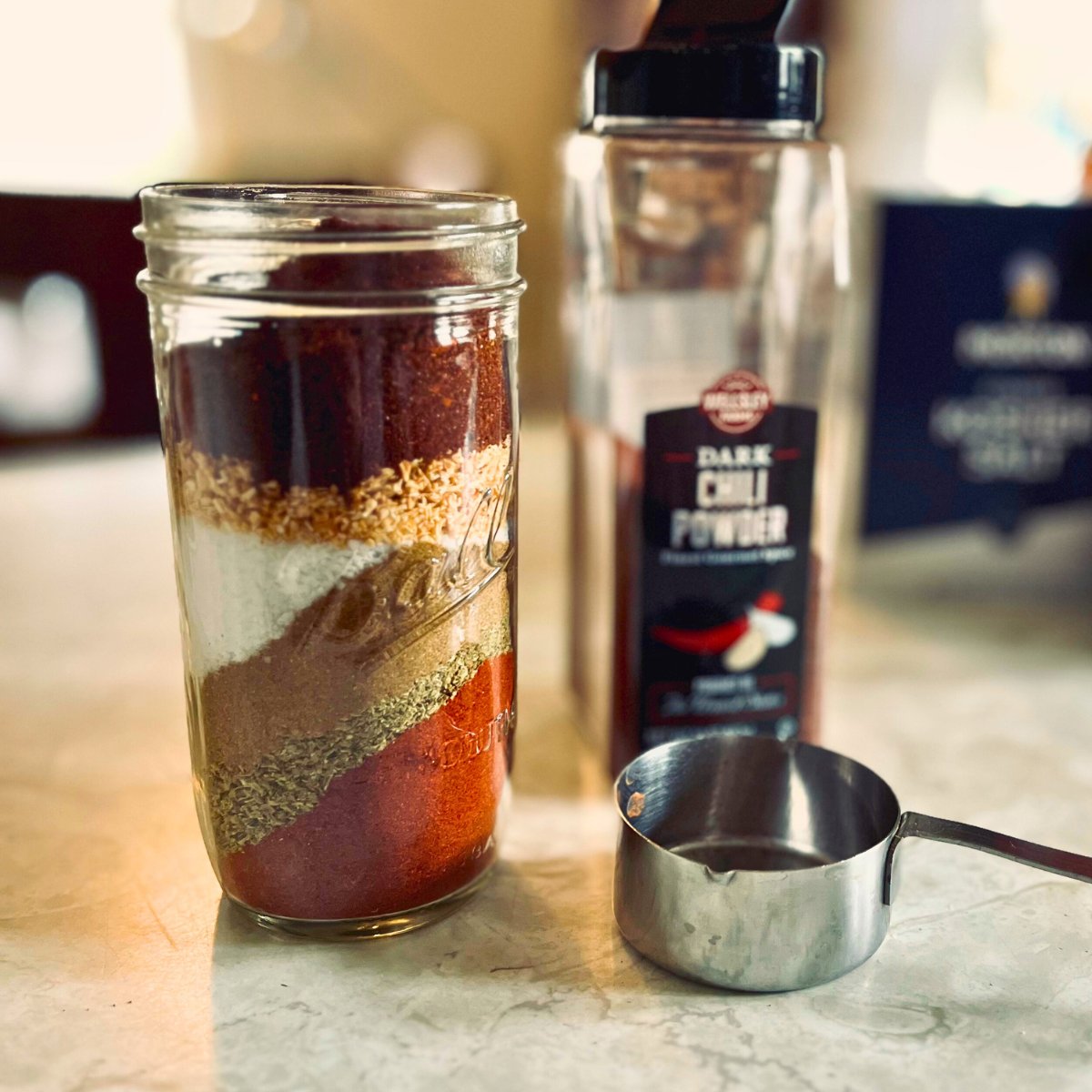 Jar of layered homemade taco seasoning next to a bottle of chili powder and a measuring cup