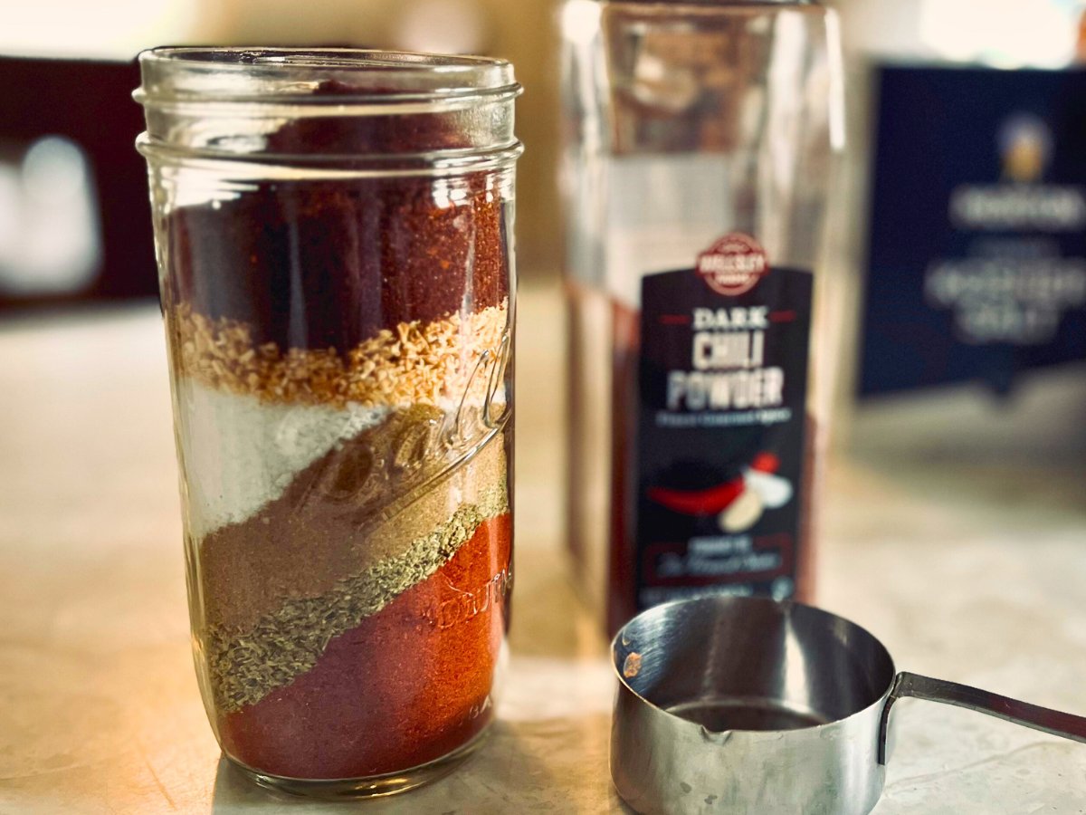 Jar of layered homemade taco seasoning next to a bottle of chili powder and a measuring cup