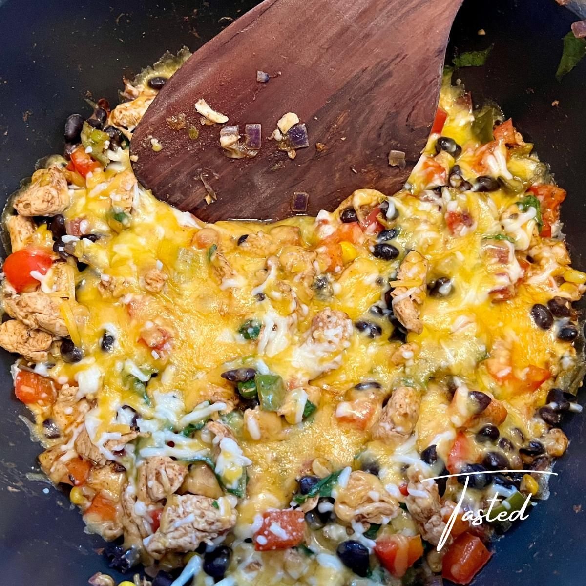 Skillet of Mexican chicken and rice with black beans, peppers and melted cheese, with a wooden spatula