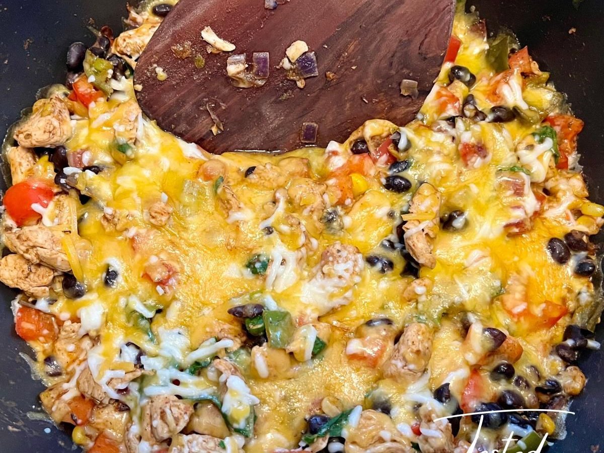 Skillet of Mexican chicken and rice with black beans, peppers and melted cheese, with a wooden spatula