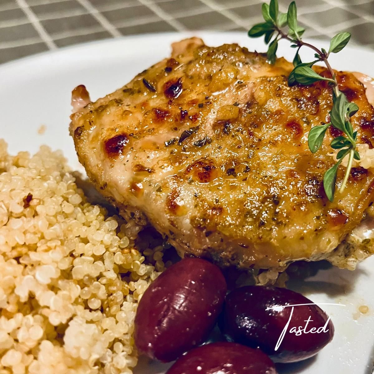 Golden Greek chicken thigh with fresh thyme on a plate with quinoa and kalamata olives