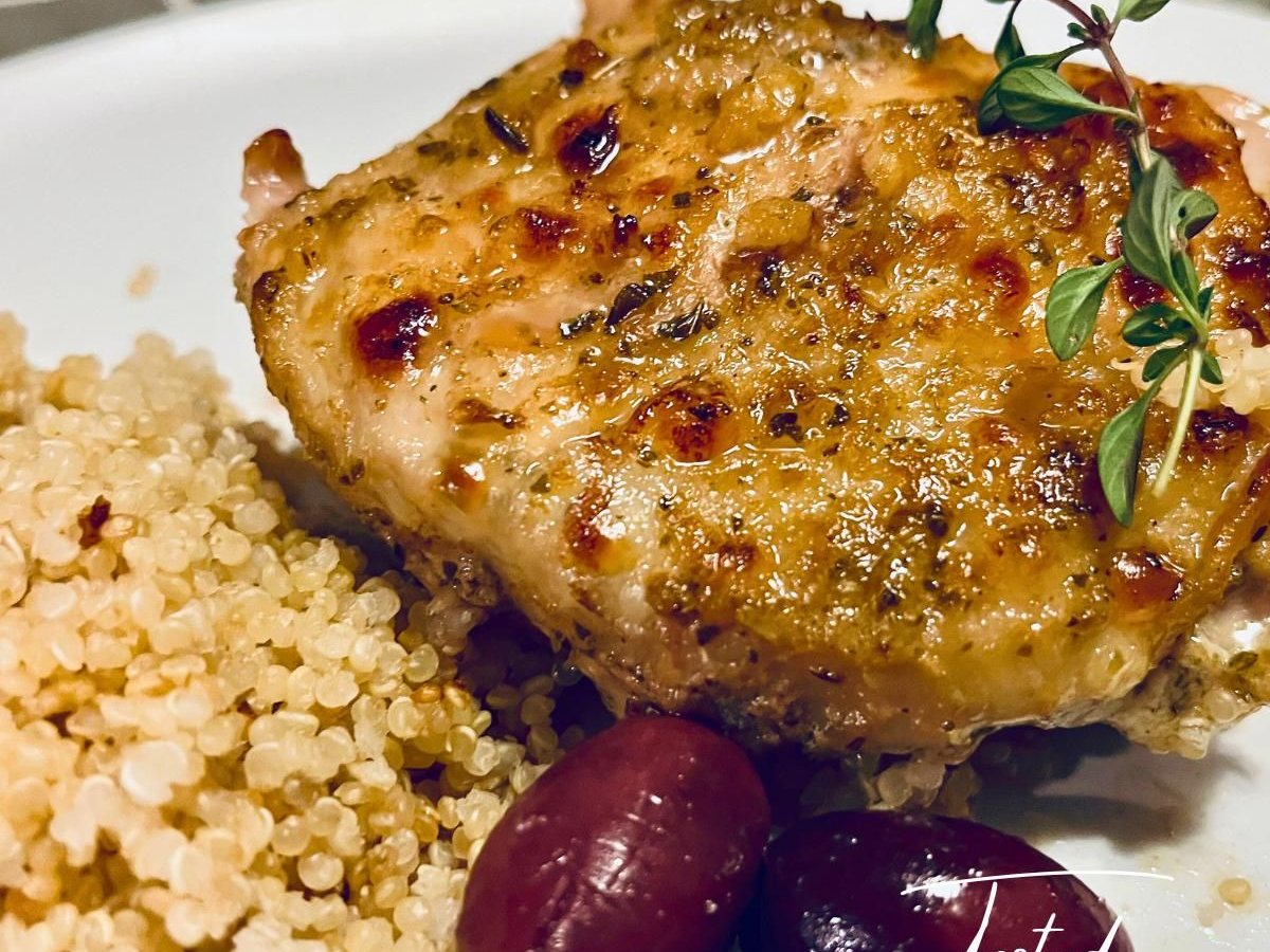 Golden Greek chicken thigh with fresh thyme on a plate with quinoa and kalamata olives