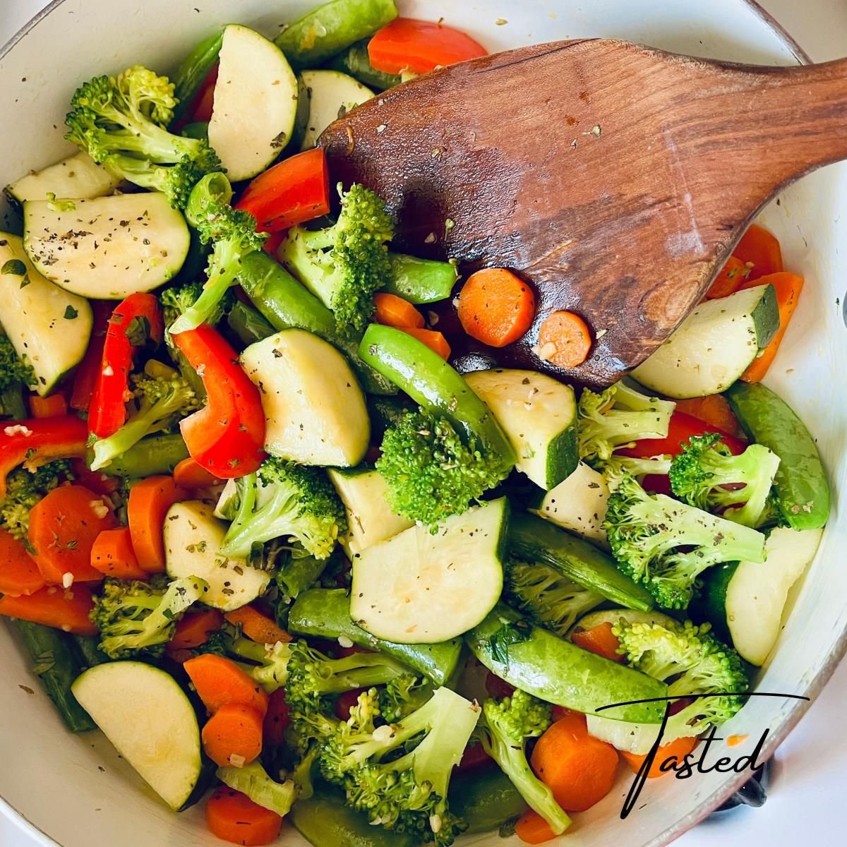 Sauteed broccoli, zucchini, carrots, snap peas and red pepper in a pan with a wooden spatula