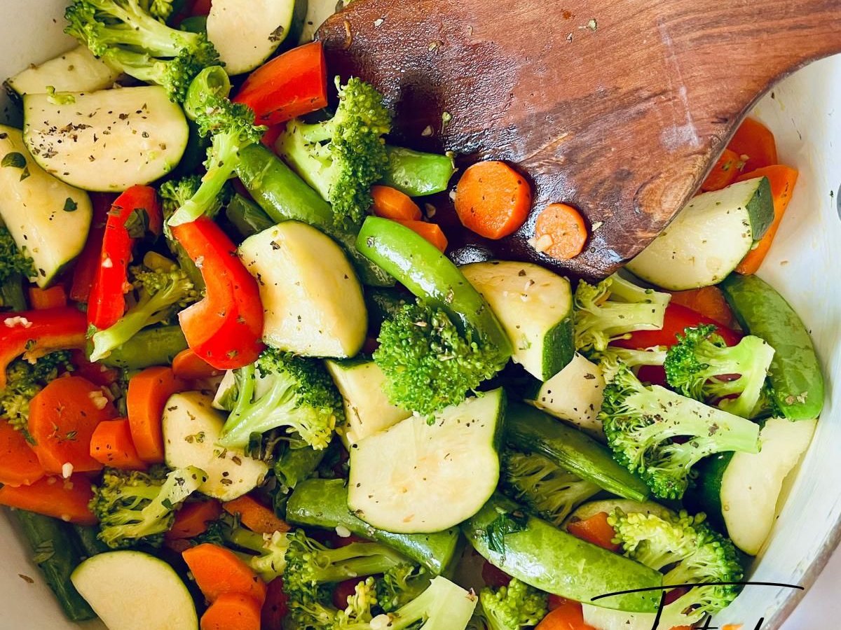 Sauteed broccoli, zucchini, carrots, snap peas and red pepper in a pan with a wooden spatula