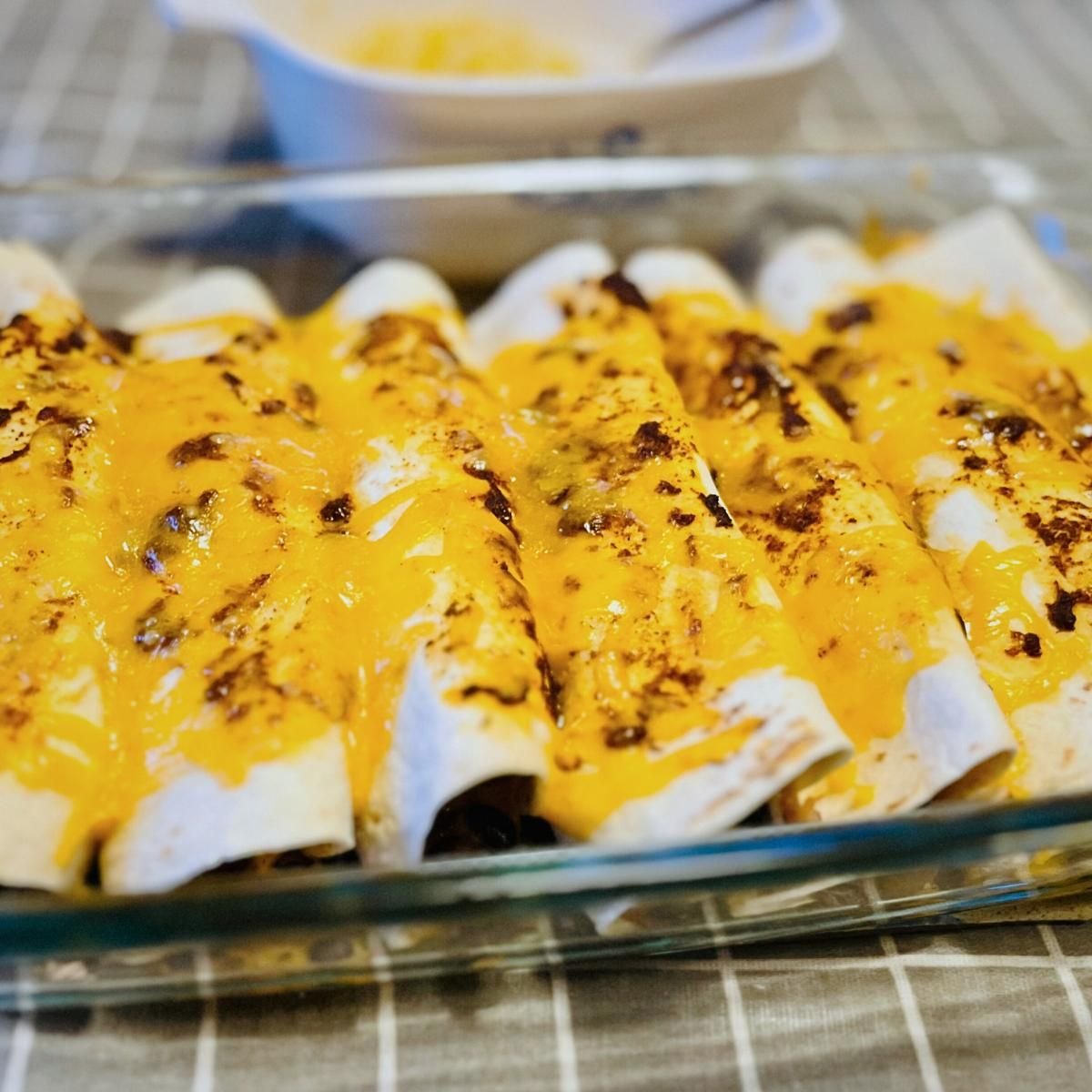 Glass baking dish of turkey enchiladas topped with melted, browned cheddar