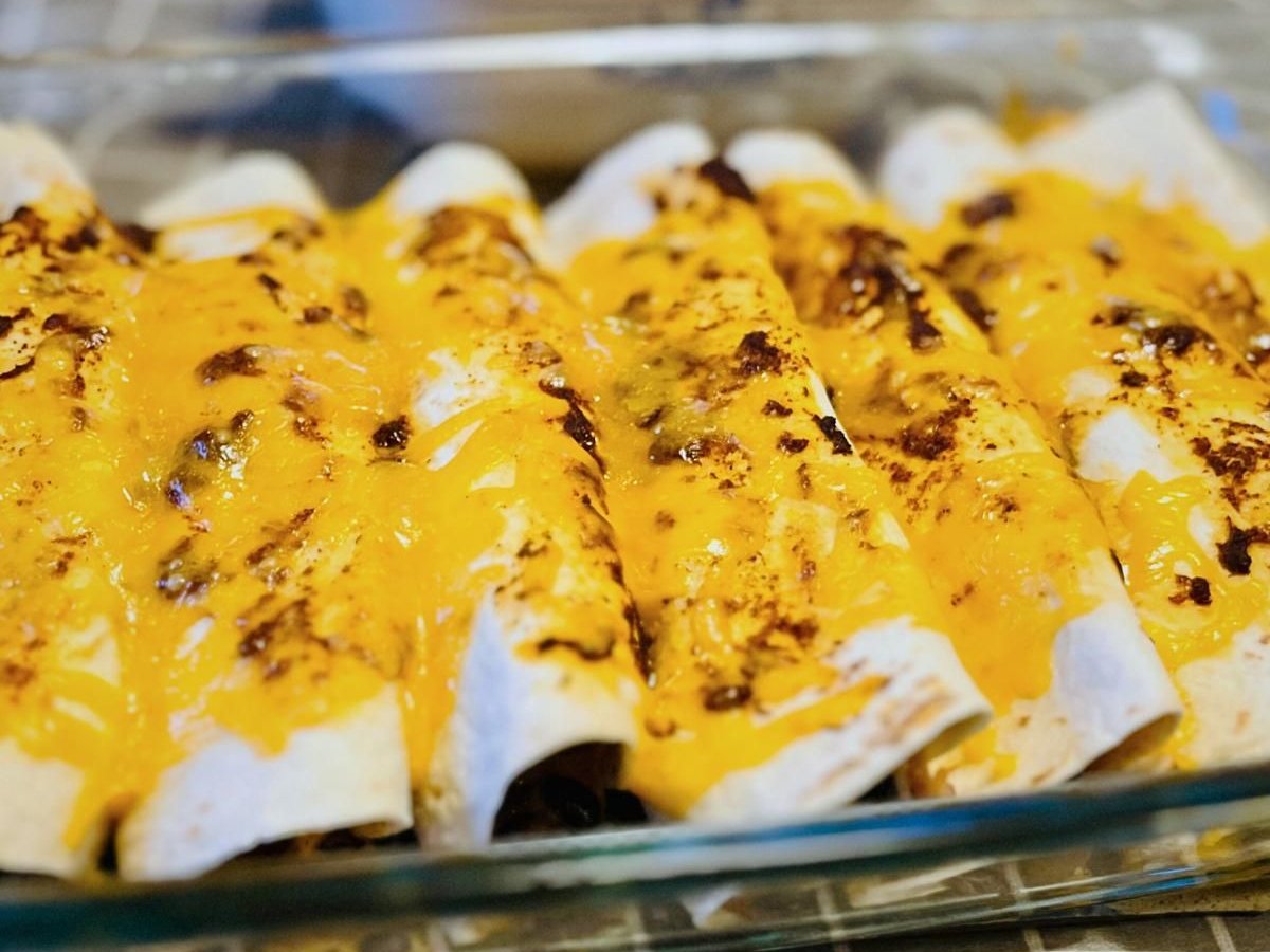 Glass baking dish of turkey enchiladas topped with melted, browned cheddar
