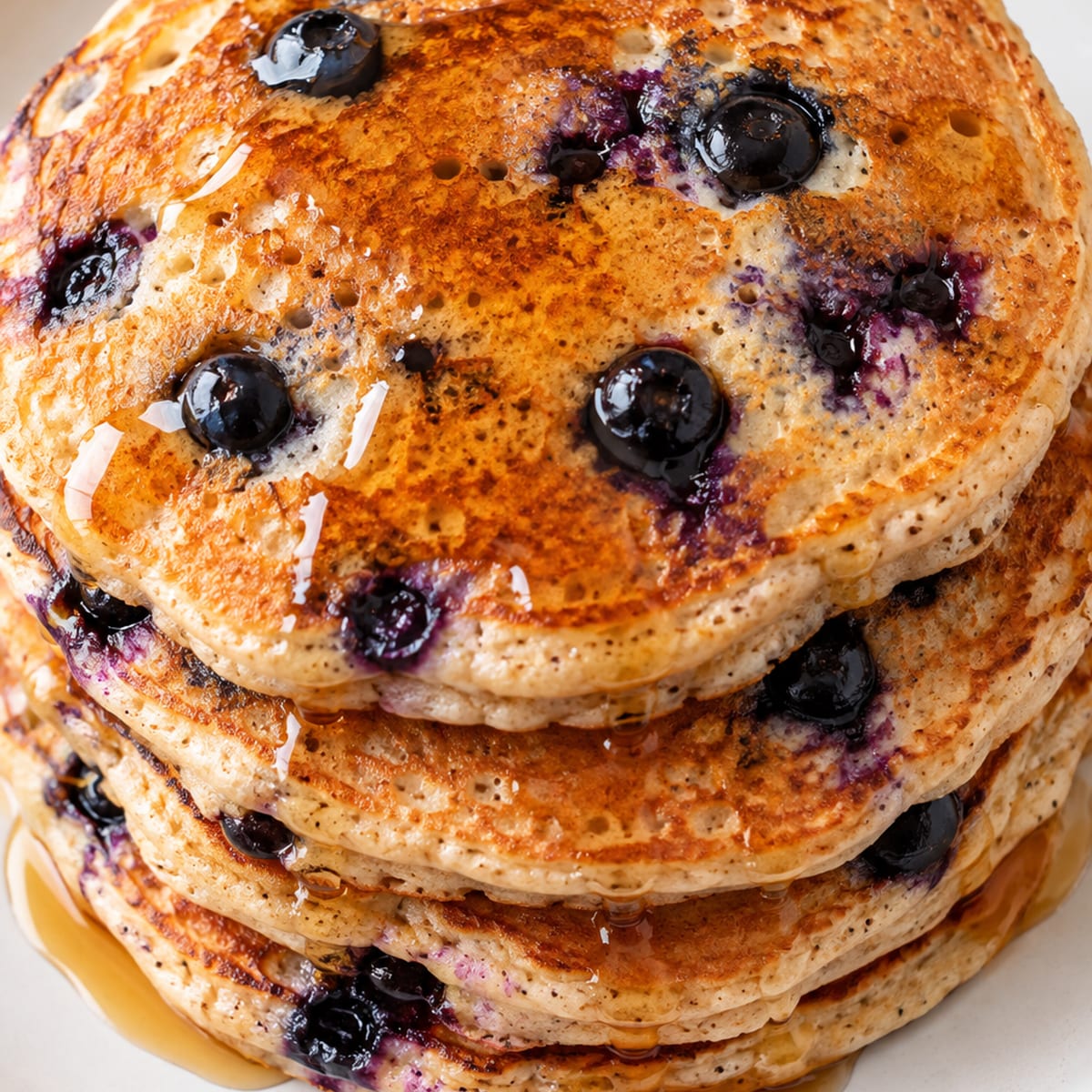 Stack of whole spelt pancakes with blueberries and maple syrup on a white plate
