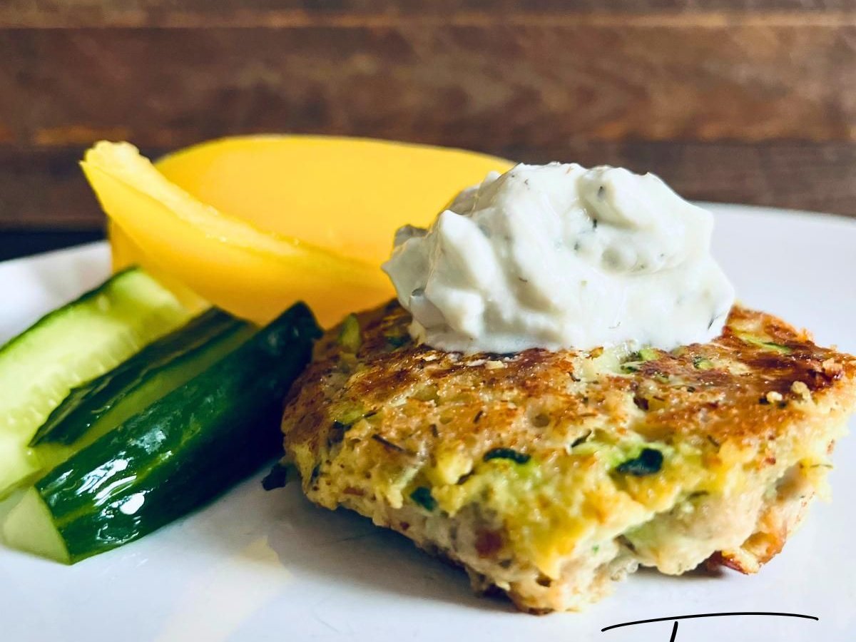 Zucchini tuna patty topped with a dollop of herbed sauce, with cucumber spears and mango slices